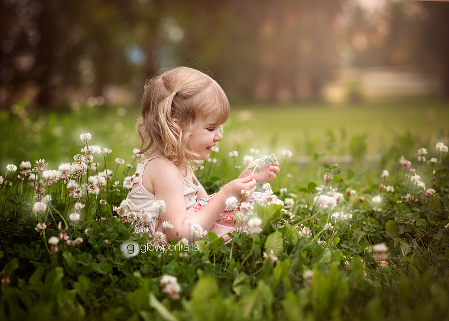 little girl sitting in flower field holding flower