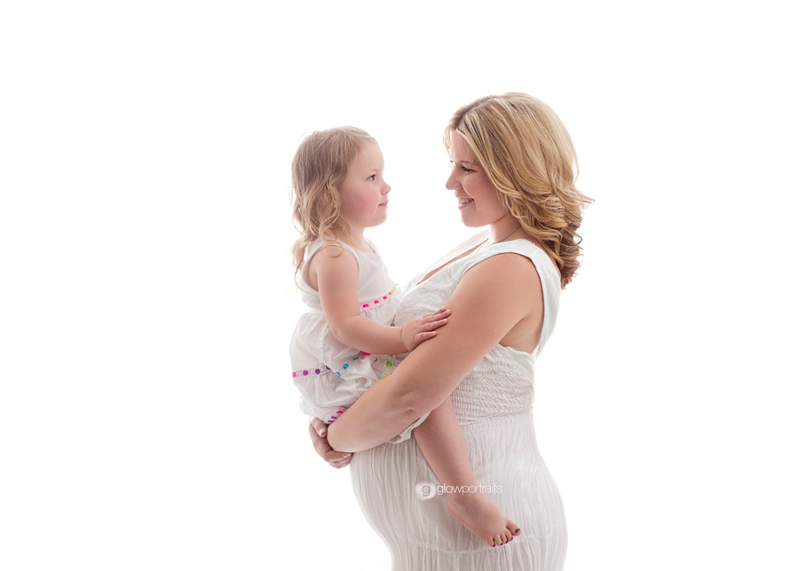 mom holding daughter in white dress for maternity pose