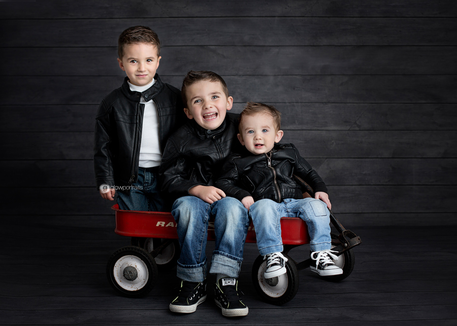 three boys wearing black leather jackets sitting on red wagon