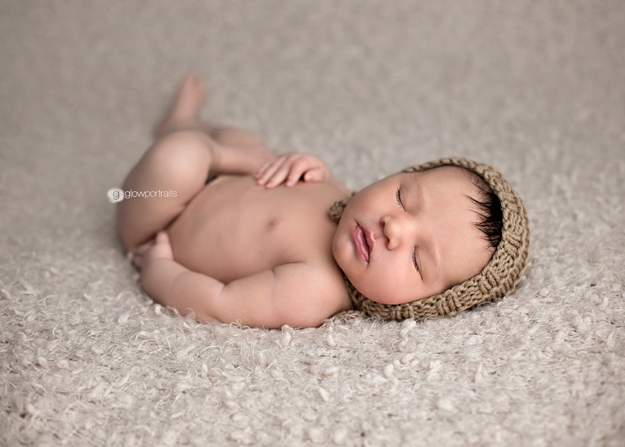 newborn boy wearing bonnet lying on back