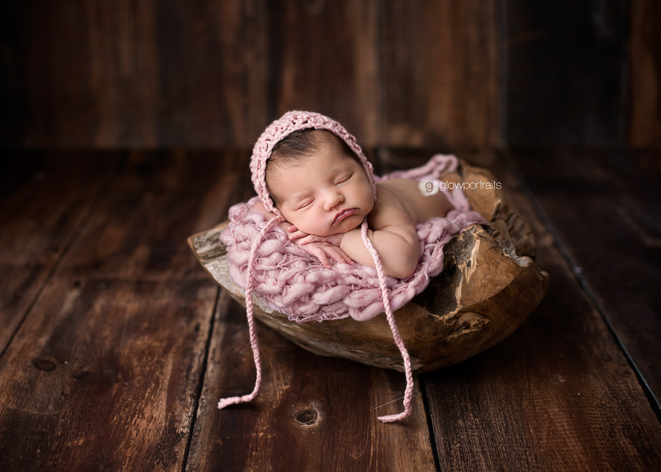 newborn baby in wood bowl with pink hat