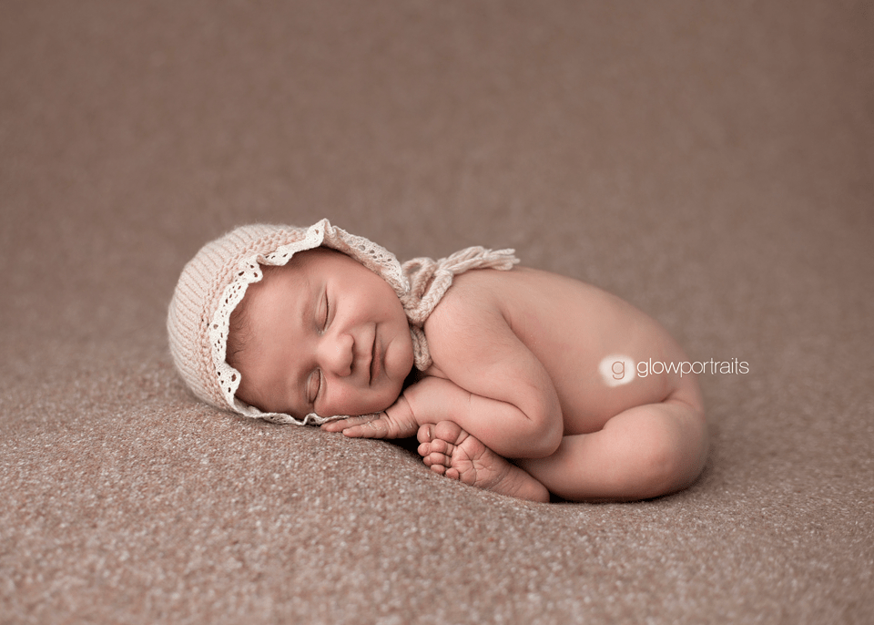 newborn girl wearing bonnet in taco pose