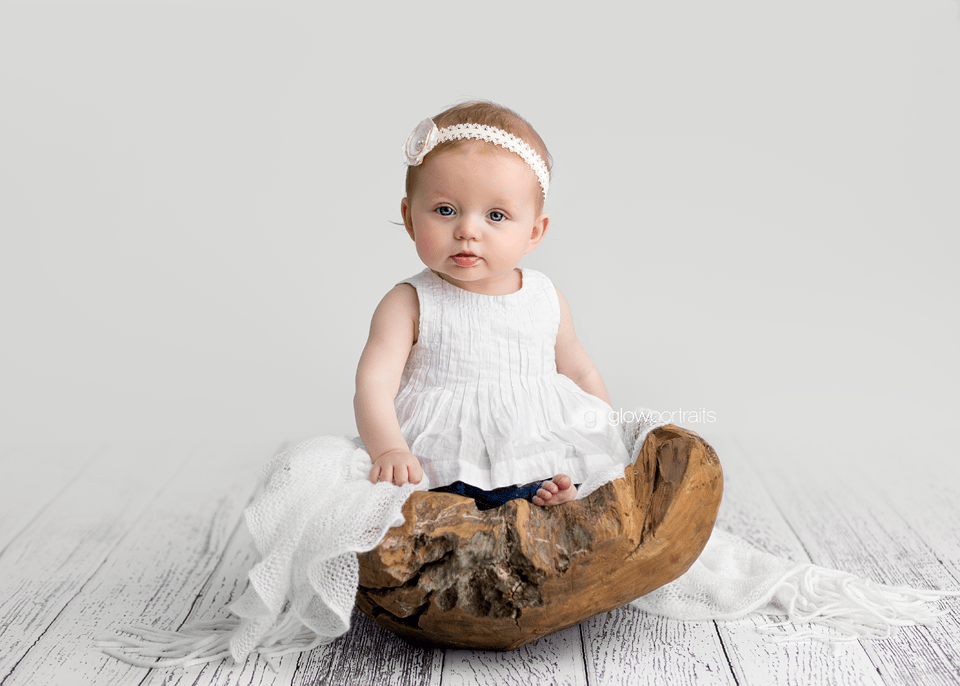 baby girl wearing white dress sitting in wooden bowl