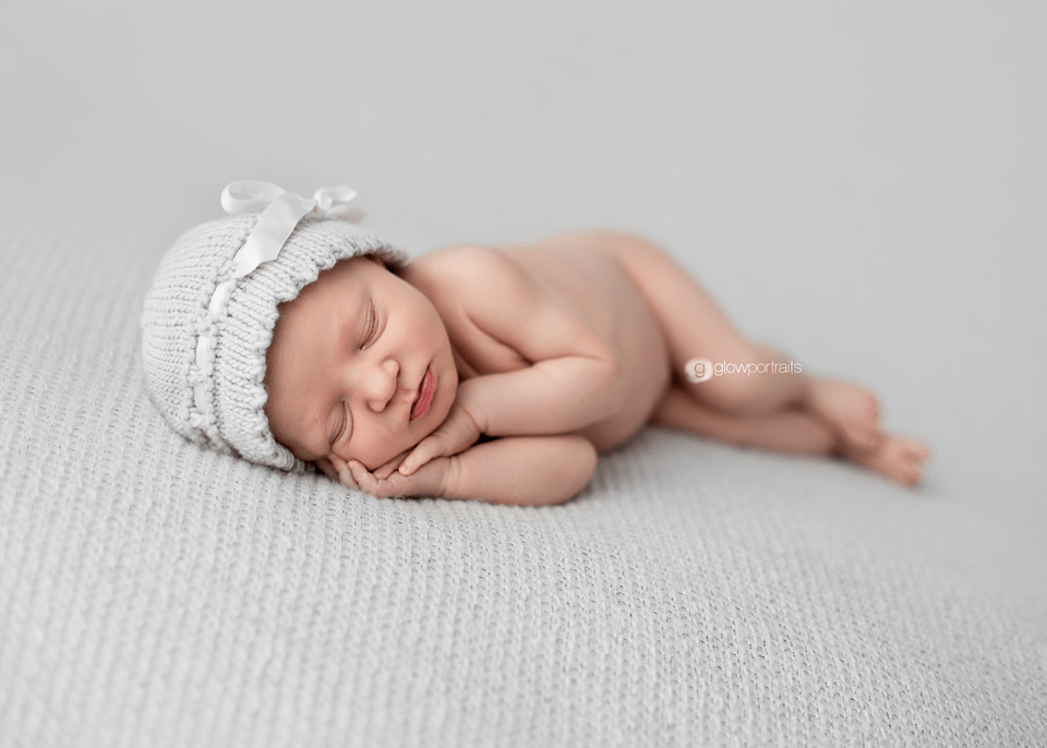 newborn baby on gray fabric wearing gray ribbon hat